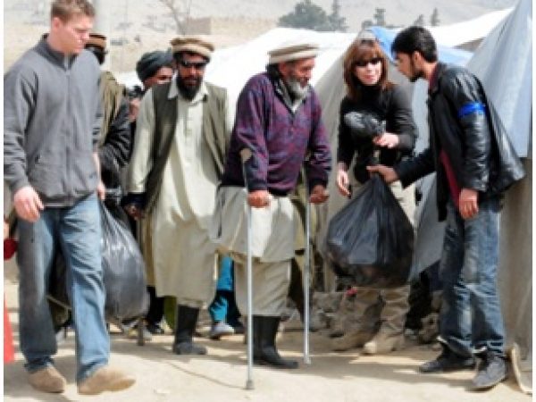 NTM-A/CSTC-A personnel help two afghan amputees with their bags of donated goods. Over 400 bags, which contained clothes, toiletry items, toys, candy, and school supplies, were distributed to several hundred Afghans who live at Qaragha refugee camp.